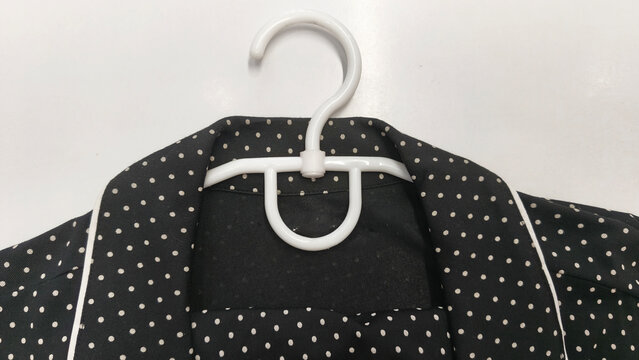 Black polka dot clothes hanging on a white plastic hanger, a garment with a classic collar, contrast trim and an elegant vintage style.