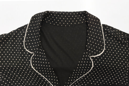 A close up of a black polka dot collar on a white background. This classic collared garment features contrasting trim and an elegant vintage style.