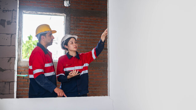 Construction engineers inspecting interior wall finishing at an unfinished building, reviewing structural quality, safety, and renovation progress for professional residential construction projects.