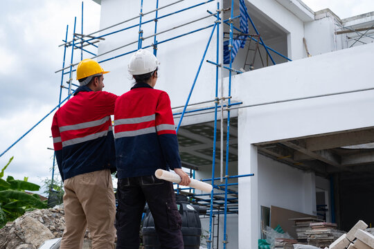 Construction engineers inspecting a modern building with scaffolding while reviewing rolled blueprints, highlighting project planning, structural safety, site supervision, quality control, teamwork.