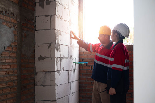 Construction engineers inspecting masonry walls inside an unfinished building while evaluating structural quality. Building inspection, renovation, teamwork, workplace safety, and quality control.