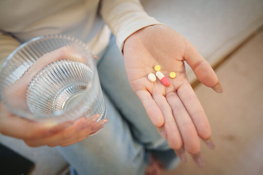 Overhead view of hand holding pills and glass of water for daily medication