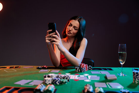 Online poker woman with a smartphone at a casino table with cards and chips.