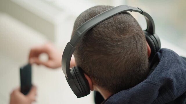 Close up of young man wearing headphones listening to music while another man holds and adjusts electronic device nearby. scene is indoors with soft lighting focusing on interaction