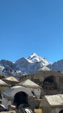 Cemit&eacute;rio hist&oacute;rico de Milluni com o pico nevado Huayna Potos&iacute; ao fundo, Bol&iacute;via. V&iacute;deo vertical de tumbas r&uacute;sticas e cruzes no altiplano andino sob c&eacute;u azul.
