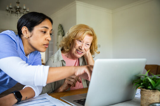 Caregiver helping senior woman with laptop at home