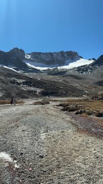 Trilha de montanha com riacho de degelo e pico nevado ao fundo nos Andes. V&iacute;deo vertical de paisagem andina em dia de sol e c&eacute;u limpo.