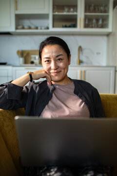 Smiling woman working on laptop in home kitchen