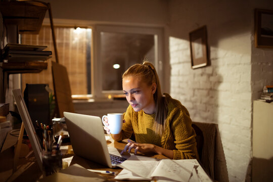 Young woman working late at home office with laptop and coffee