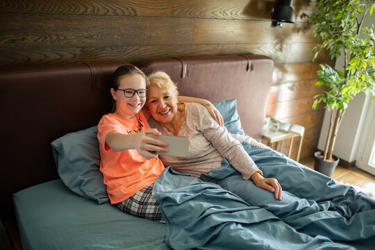 Smiling grandmother and granddaughter taking selfie in bed at home