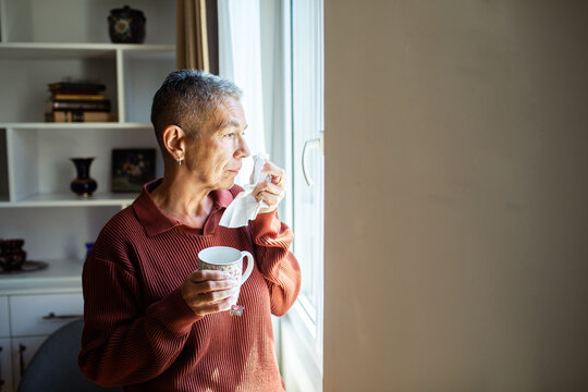 Senior woman holding tissue and tea by home window
