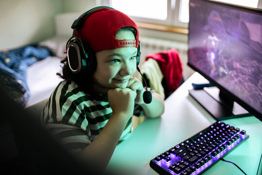 Smiling teen gamer with headset playing pc game at home