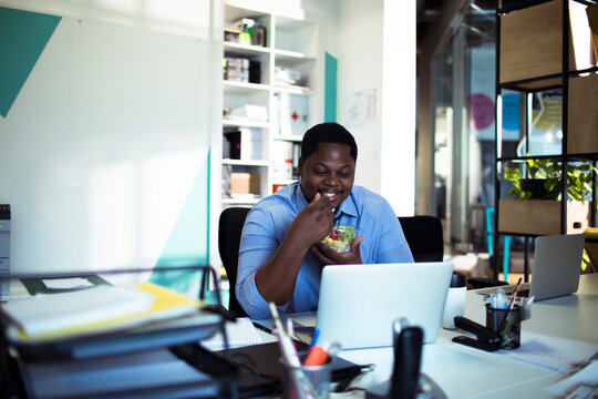 Smiling man eating healthy lunch at office desk