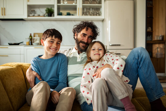 Father with son and daughter relaxing on sofa in home kitchen