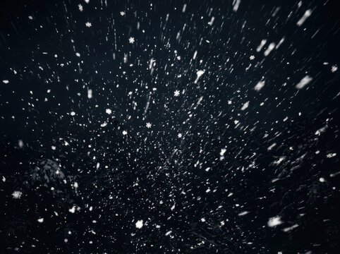 Bright white snow flakes falling down against a dark black winter night background