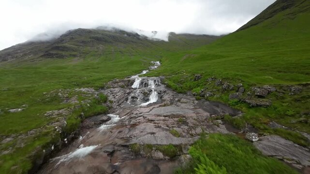 FPV flying up cascading river on side of Glencoe mountain Scotland