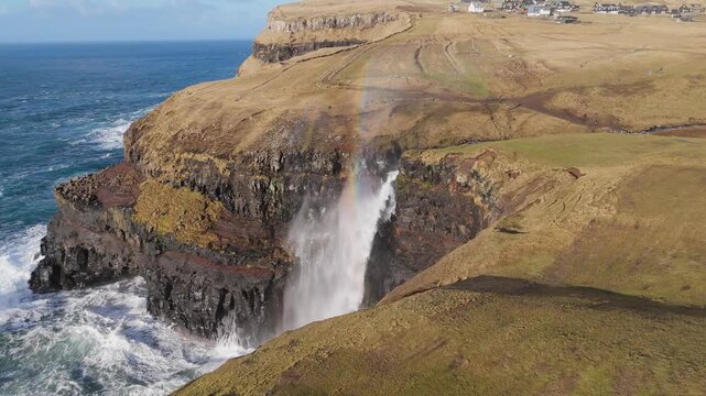 フェロー諸島ガーサダルル、断崖から海へ落ちるムーラフォッスルの滝と虹を空撮（Mulafossur Waterfall Gasadalur Faroe Islands Aerial 4K）