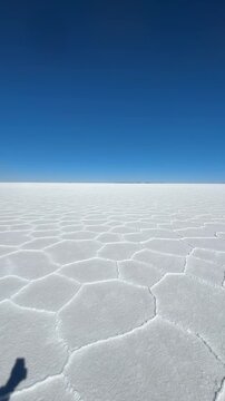 Vista panor&acirc;mica das padronagens geom&eacute;tricas de sal seco no Salar de Uyuni, Bol&iacute;via. V&iacute;deo vertical de horizonte infinito no deserto de sal sob c&eacute;u azul.