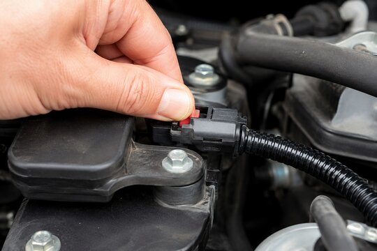 Mechanic hand releasing electrical connector locking tab during routine vehicle engine maintenance