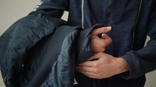 Close up of man holding and adjusting his dark blue jacket revealing its texture details like stitching patterns and zipper. man wears matching navy clothing with subtle white piping