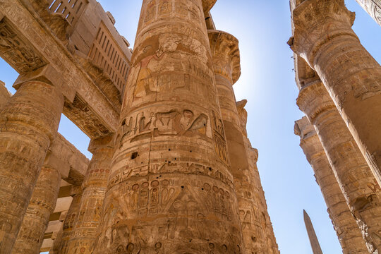 Majestic view of ancient Egyptian Great Hypostyle Hall featuring towering stone columns adorned with intricate historic hieroglyphics under bright blue desert sky