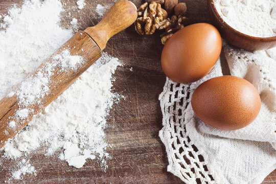 Baking ingredients on a rustic wooden board, including a rolling pin covered in white flour, fresh brown eggs, and walnuts , representing homemade cooking. Copy space