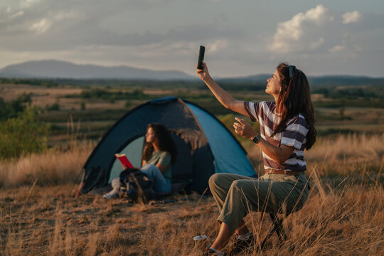 Young women camping outdoors using smartphone for connectivity