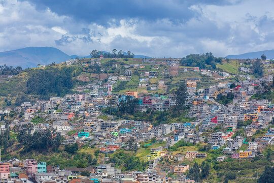 Colorful colorful houses and dense residential buildings built on the hillside slopes in Quito, Ecuador, against Andean mountain background.