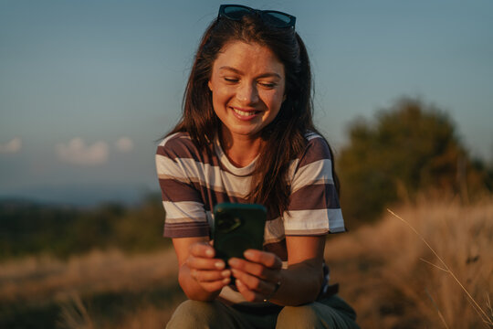 Young woman smiling using smartphone outdoors at sunset