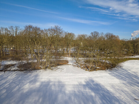 Aerial view of a snow-covered park with bare trees and a frozen pond under a clear blue sky in Berlin, Berlin, Germany.