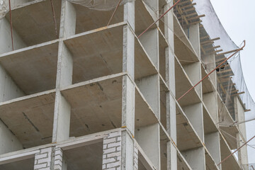 Construction progresses on a modern building reaching for the sky amidst a gray cloudy backdrop © beholdereye
