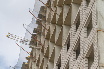Construction site shows the towering building frame in urban landscape during bright daylight with cranes and safety nets © beholdereye