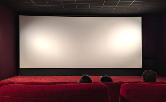 Empty cinema screen with group of people sitting in red seats before a movie begins