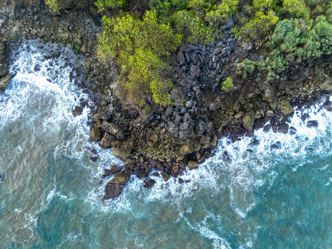 Aerial view of rugged rocky coastline with crashing waves and lush green vegetation along the shore in Pacitan, East Java, Indonesia.
