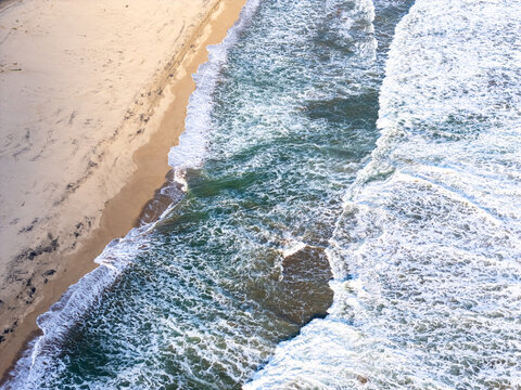 Aerial view of the sandy coastline with turquoise waves crashing onto the shore in Pacitan, East Java, Indonesia.
