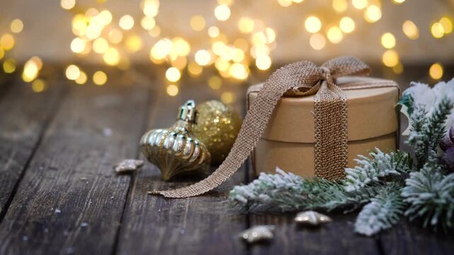 A natural kraft paper gift box tied with a burlap ribbon sits on weathered wood beside golden ornaments and frosted pine, as warm lights twinkle behind for a cozy, rustic holiday feel.