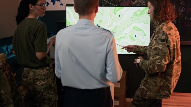 Caucasian military officers analyzing digital map on screen in command center, tilting up from desk. Perfect for defense industry marketing or national security videos