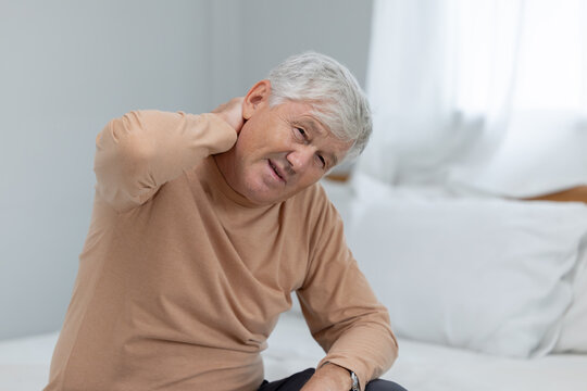 Older man sitting on bed holding his neck in pain  suffer from neck pain during morning