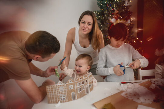family with children cutting out paper Christmas tree ornaments in living room. A cozy weekend, time spent with the kids. Blurry, out-of-focus photos, background, lifestyle, live photos, real people
