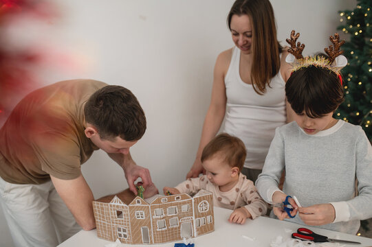 family with children cutting out paper Christmas tree ornaments in living room. A cozy weekend, time spent with the kids. Blurry, out-of-focus photos, background, lifestyle, live photos, real people