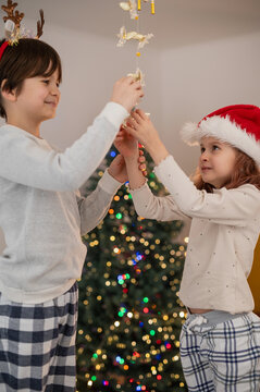 Brother and sister children decorate the house for Christmas, wind chimes and bells with angels vertical