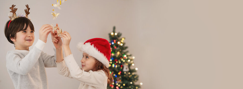 Brother and sister children decorate the house for Christmas, wind chimes and bells with angels banner copy space