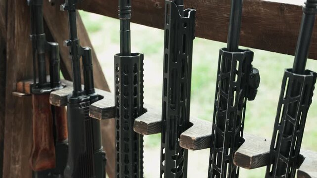Close-up of several modern rifles standing side by side in a firearm rack at a shooting range.