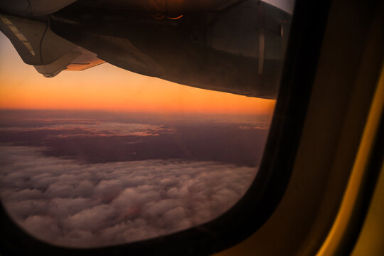 Aerial view of the airplane wing silhouetted against a vibrant sunset over a thick layer of clouds during a flight in Madagascar.