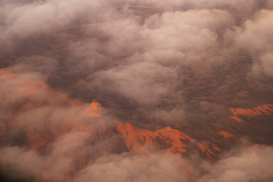 Aerial view of rugged mountainous terrain partially obscured by clouds during golden hour, Madagascar.