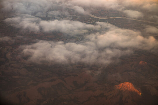 Aerial view of the rugged mountainous landscape of Madagascar during golden hour, with soft clouds drifting over the terrain and warm sunlight highlighting the peaks, Madagascar.