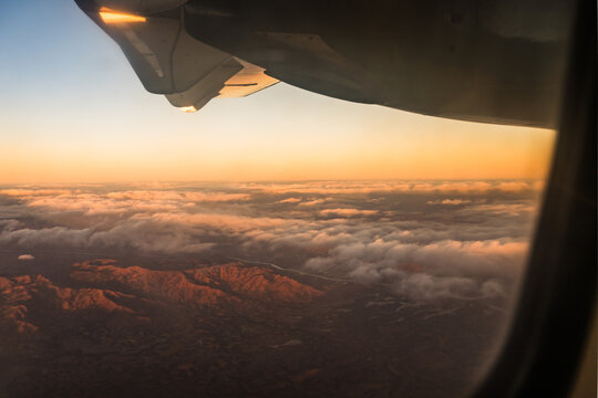 Aerial view of the mountainous landscape of Madagascar at sunset, seen from an airplane window with the wing visible above a layer of clouds, Madagascar.