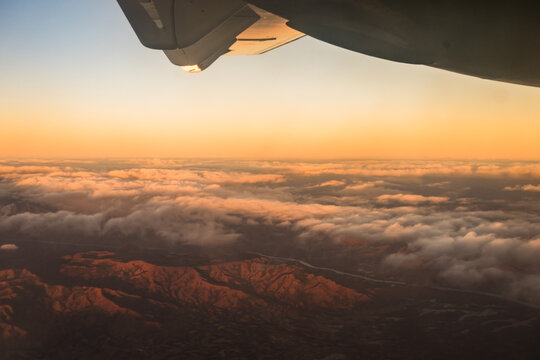 Aerial view of mountainous landscape at sunset with clouds and an airplane wing visible over Madagascar.