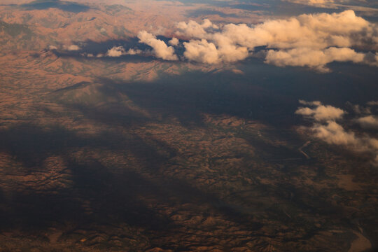 Aerial view of the rugged mountainous landscape during a flight, featuring rolling hills, deep shadows, and scattered clouds illuminated by golden hour light Madagascar.