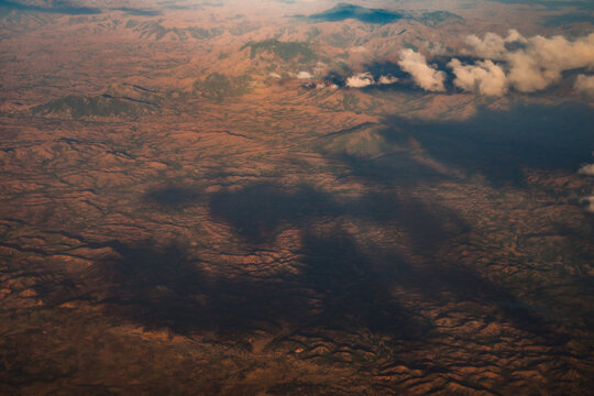 Aerial view of the rugged mountainous landscape with rolling hills, deep valleys, and scattered clouds casting shadows over the terrain in Madagascar.